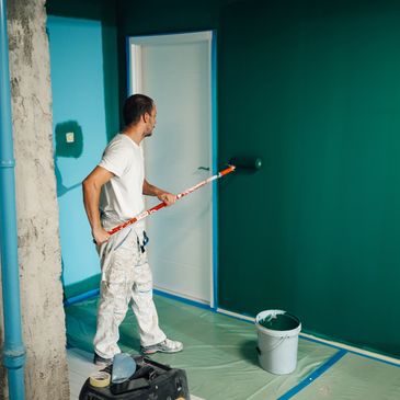 Man painting a wall teal with a roller in a partially renovated room.