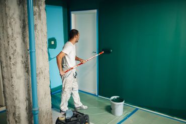 Painter in protective suit preparing to paint a wall with a ladder.