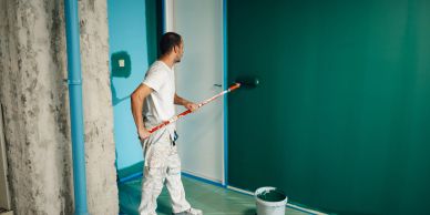 A man painting a wall teal with a roller.
