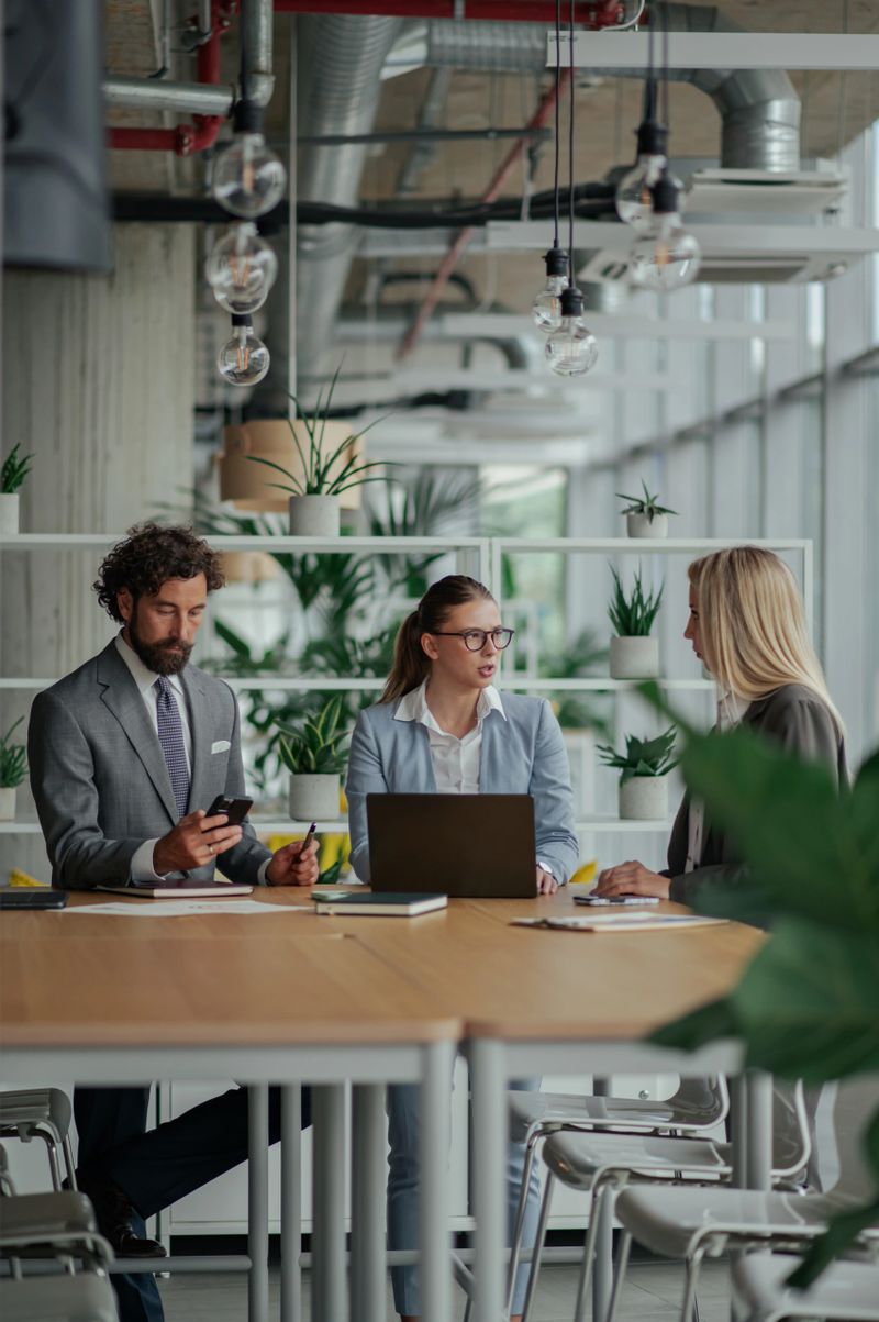 Businesspeople are having a meeting in a modern office, using laptop and smartphone, surrounded by plants