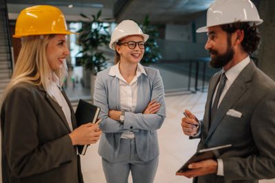 Three professionals in safety helmets discussing a project indoors.
