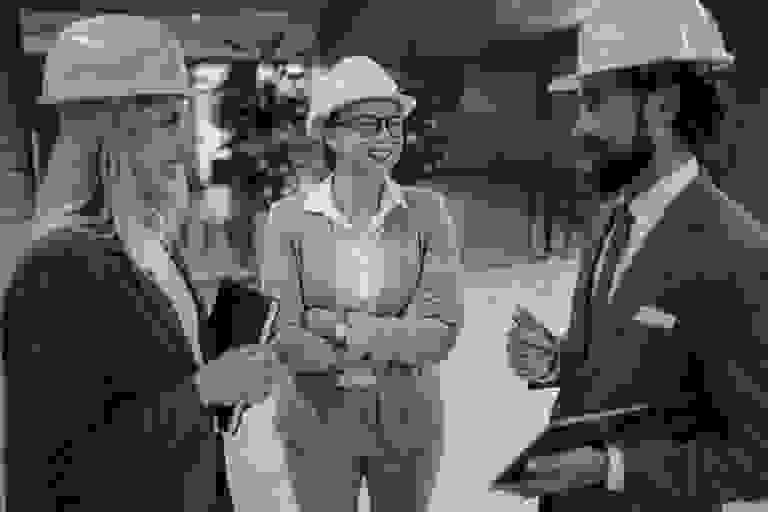 Three professionals in safety helmets discussing a project indoors.