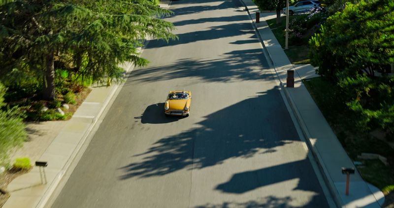 Aerial shot of a classic yellow convertible from the early 1970s driving along a residential street
on a sunny afternoon in Ventura County,  California.