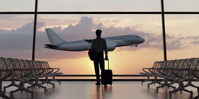 A traveler watches a plane take off at sunset from an airport lounge.