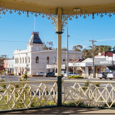 View of a quaint town street framed by a decorative gazebo railing on a sunny day.