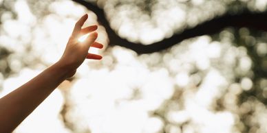 A hand reaching towards sunlight with a blurred natural background.