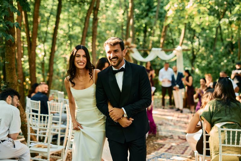 Bride and groom are smiling and walking down the aisle after getting married in a beautiful outdoor forest wedding ceremony with family and friends watching