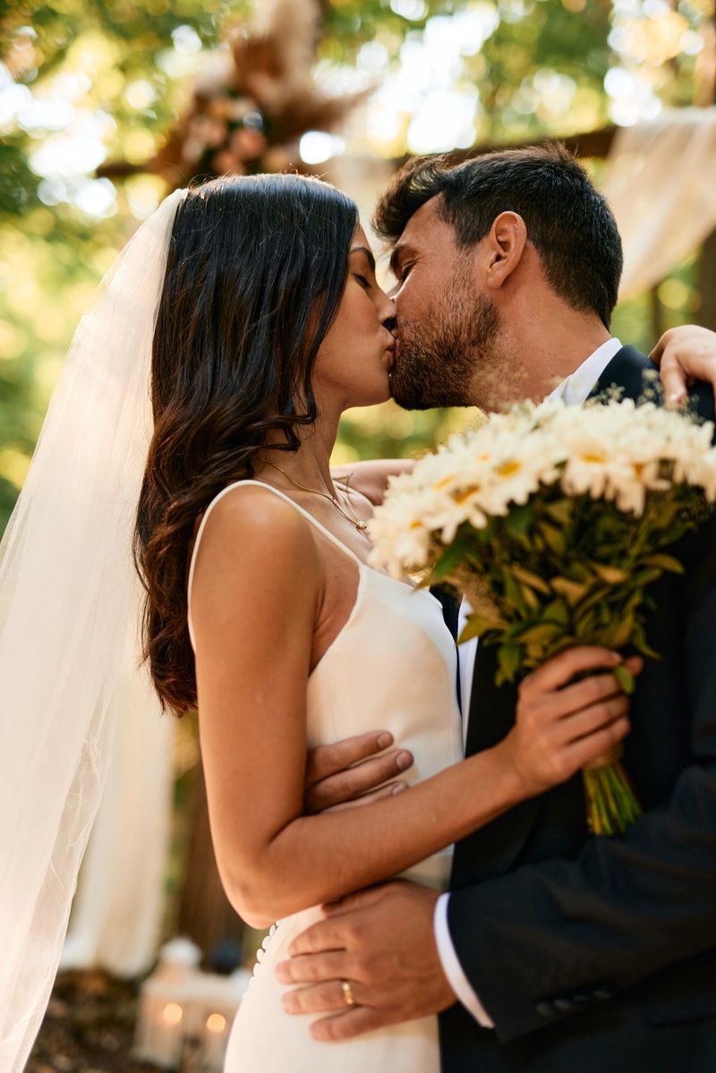 Romantic couple sharing a kiss during their outdoor wedding ceremony, enveloped by the stunning beauty of nature, celebrating their love and commitment in a serene forest setting