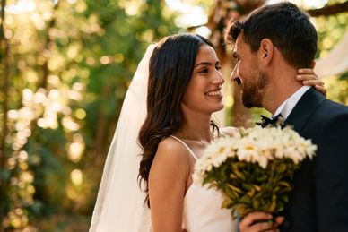 Bride and groom smiling at each other outdoors.