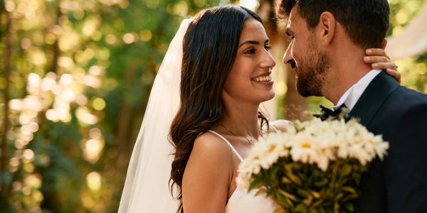 Bride and groom smiling at each other during outdoor wedding.