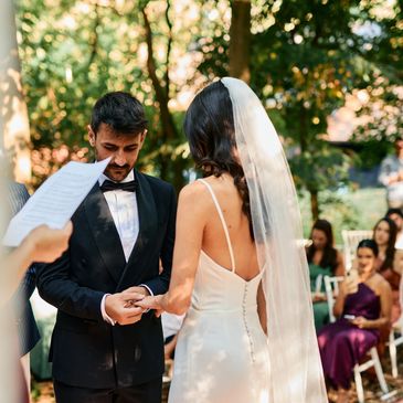 Couple exchanging rings during an outdoor wedding ceremony.