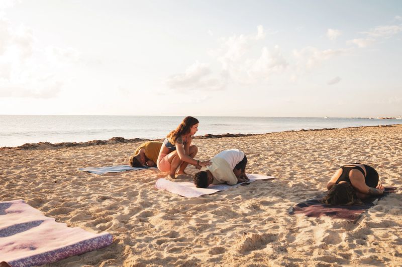 Yoga instructor guiding students in child's pose on the beach at sunrise, promoting wellness and mindfulness