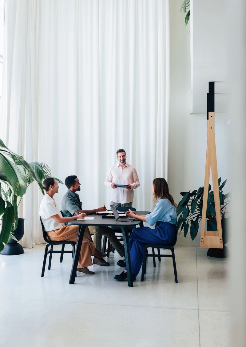 Professional group of colleagues collaborate in a contemporary office setting with stylish decor, vibrant natural light, and greenery, promoting teamwork, productivity, and a harmonious work environment.