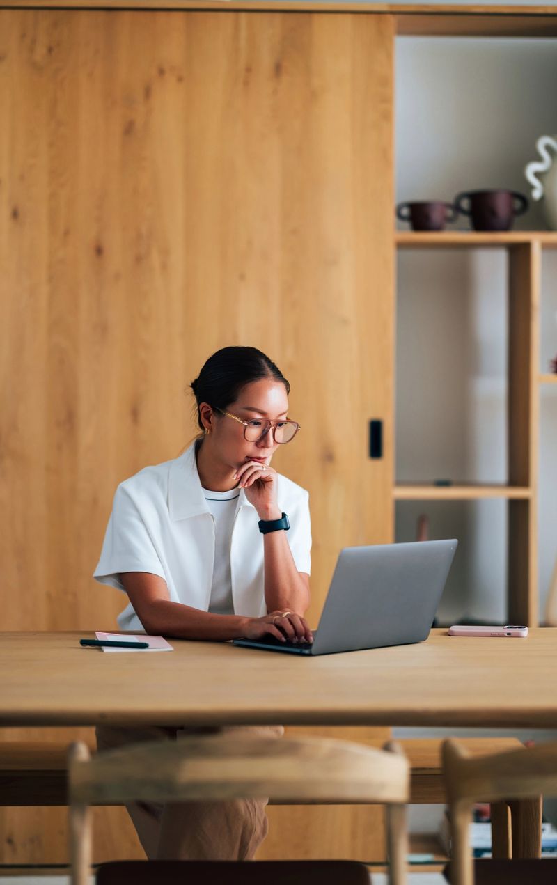 Professional businesswoman in a serene office space using her laptop for work, surrounded by modern furniture, showcasing focus, productivity, and professionalism, suitable for business or workspace-related themes.