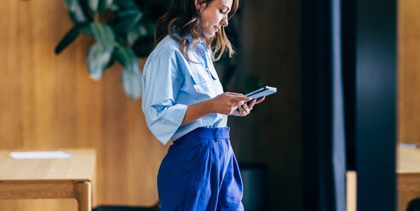 Woman standing indoors, using a tablet.