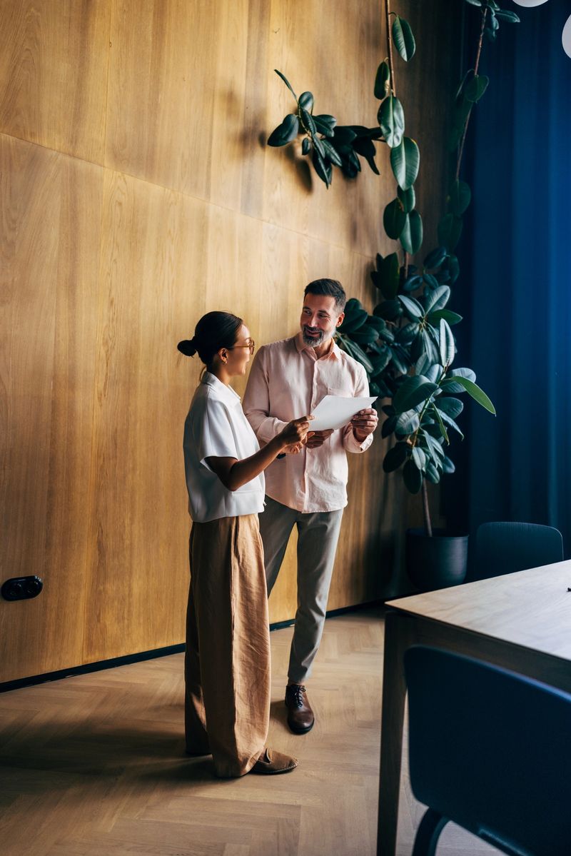 Two professionals discuss work-related tasks in a modern office space, highlighting teamwork, collaboration, and productivity in a contemporary corporate setting.