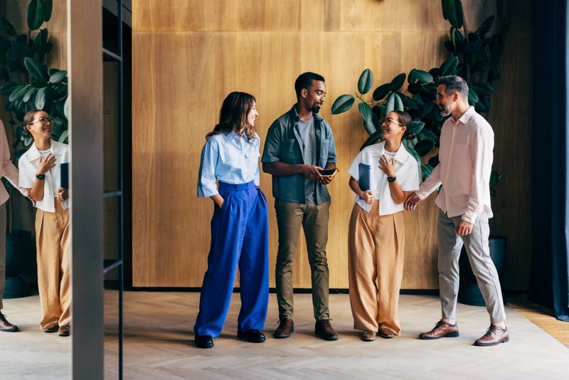 A vibrant group of colleagues sharing conversations and laughter in a contemporary office, fostering teamwork and collaboration vibes. The design reflects modern aesthetics and promotes an engaging work environment.