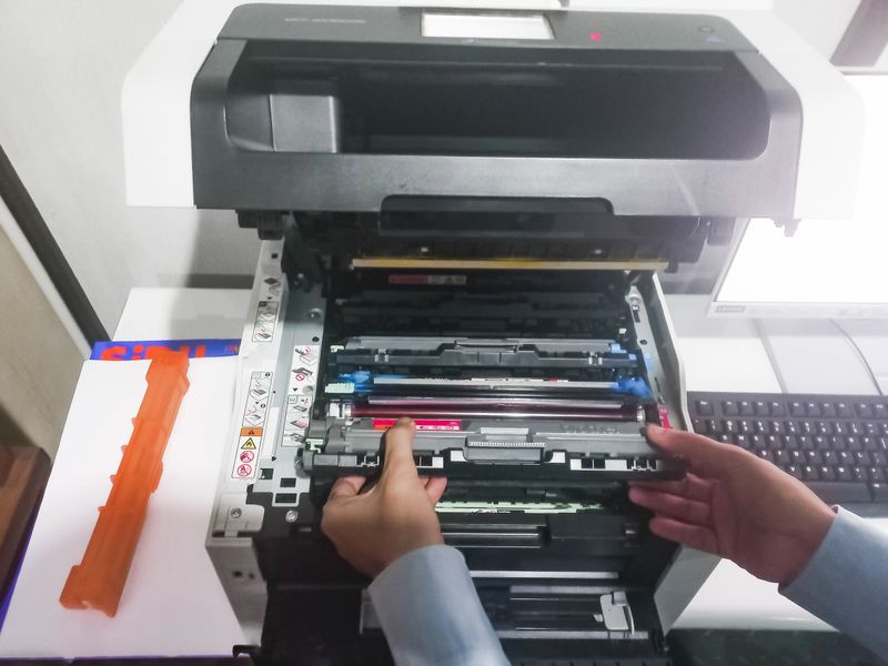 A man takes out a cartridge from a color laser printer for maintenance and refilling toner. A man is reloading the printer cartridges of a color laser jet printer.