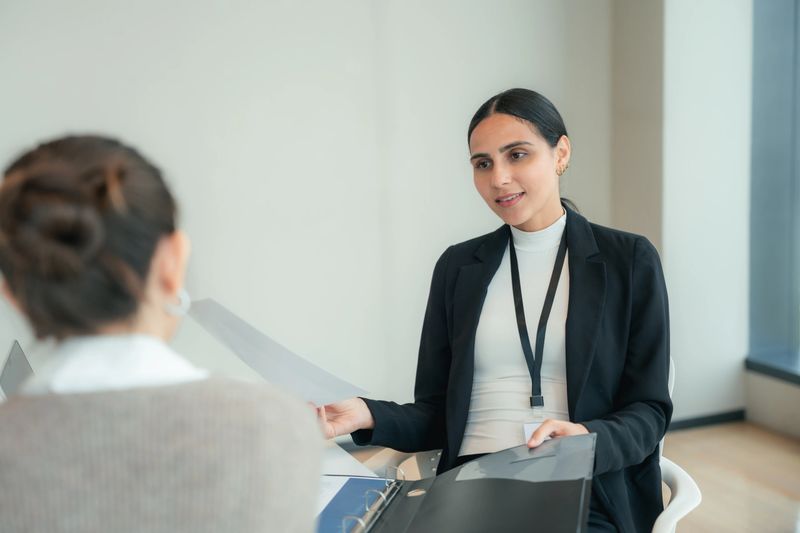 Young female first jobber confidently introducing herself to the manager in the meeting room during her first job interview with a polite handshake, confidently presenting offering a polite handshake and presenting her resume and files to highlight her preparedness and enthusiasm for the role