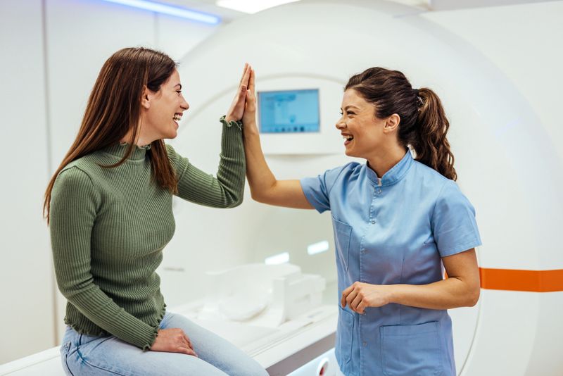 Healthcare worker in uniform sharing a celebratory high-five and smile with a patient seated next to an MRI machine. Symbolizes trust, success, and positive patient-caregiver interactions in a diagnostic healthcare setting.