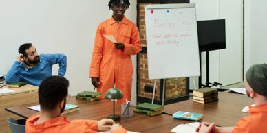 Inmates in orange jumpsuits participate in a classroom session inside a prison.