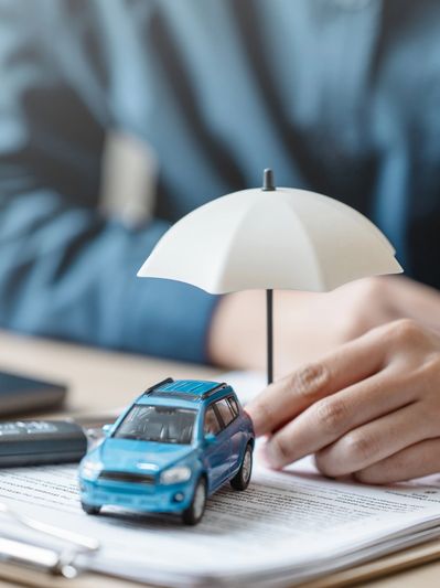 A miniature blue car under a small white umbrella symbolizing car insurance protection.