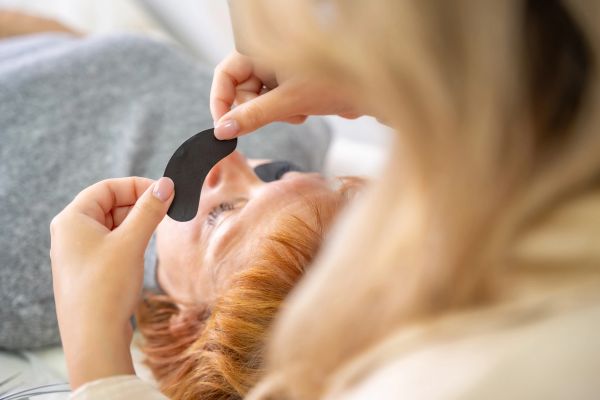 A person applying a black under-eye patch to another person's face.