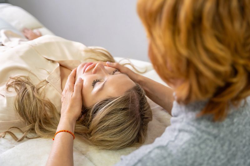 Hands of a female practitioner positioned on the face of a young woman during Access Bars facial lifting session. Concept of energy work, healing touch and alternative face therapy. High quality photo