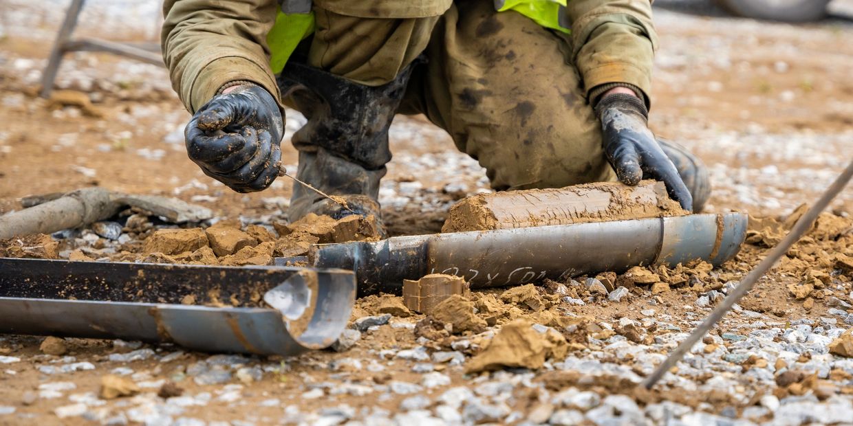 Person in protective gloves handling a large, muddy artillery shell outdoors.