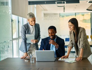 Three professionals collaborating around a laptop in a modern office.
