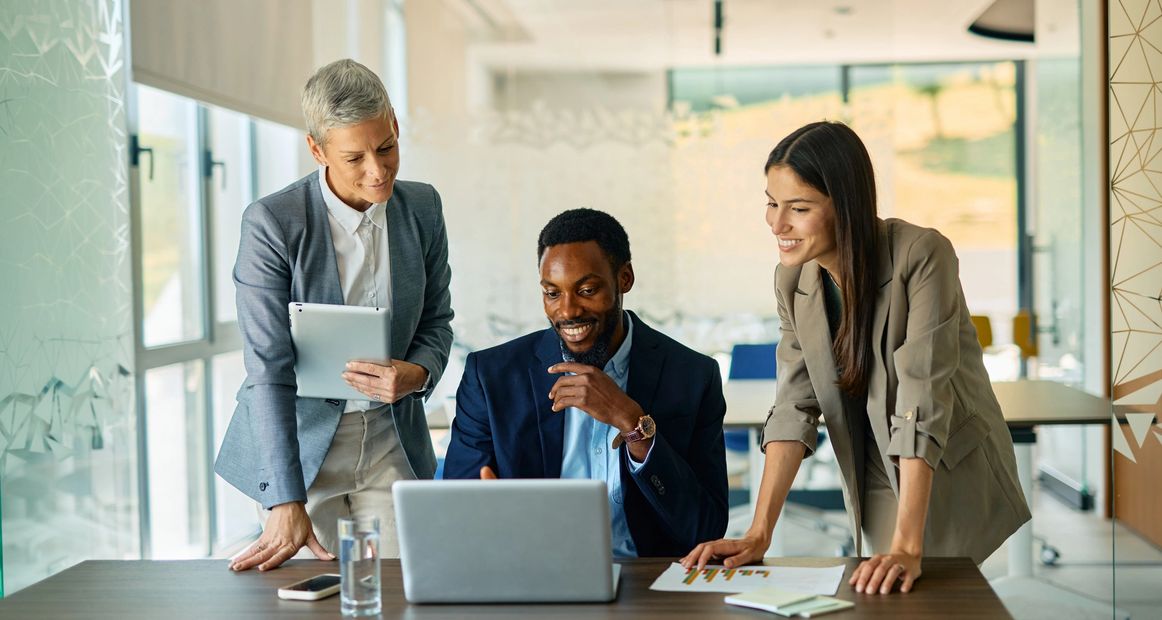 Three professionals collaborating happily around a laptop in a modern office.