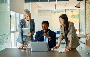 Three professionals collaborating around a laptop.
