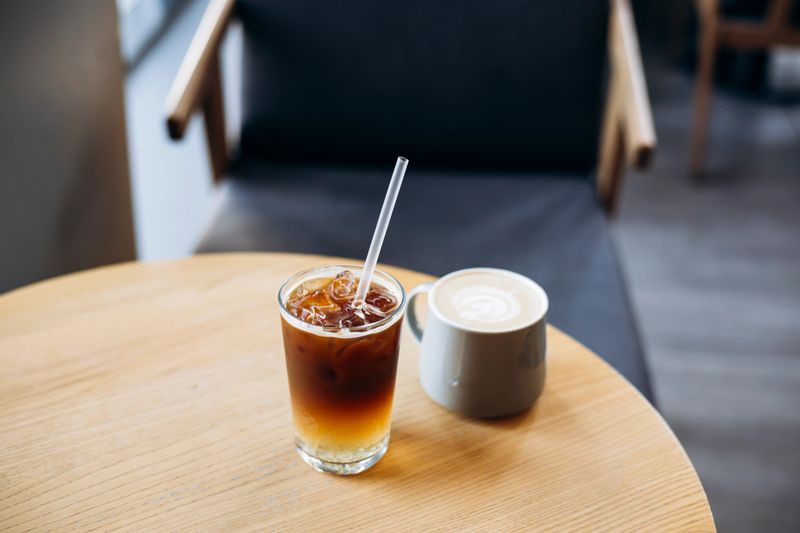 Two stylish coffee drinks â espresso tonic and cappuccino â served on a wooden table in a warm, inviting cafe interior. Perfect combination of refreshing and creamy beverages for coffee lovers.
