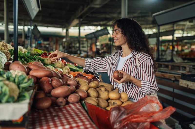 Young woman buying potatoes and other fresh vegetables at a farmers market, enjoying healthy local produce