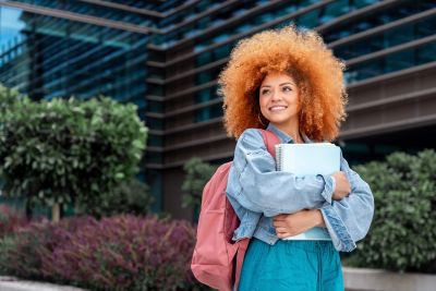 Smiling student with books and backpack outdoors.