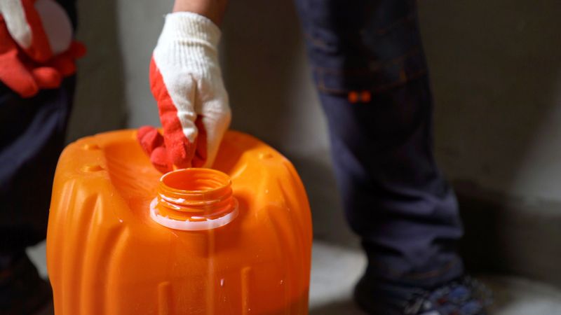 Construction worker wearing protective gloves opening an orange plastic jerrycan on a construction site