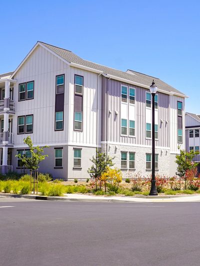 Modern three-story apartment building with white siding and multiple windows.