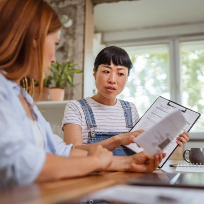 Two women discussing documents at a table in a bright room.