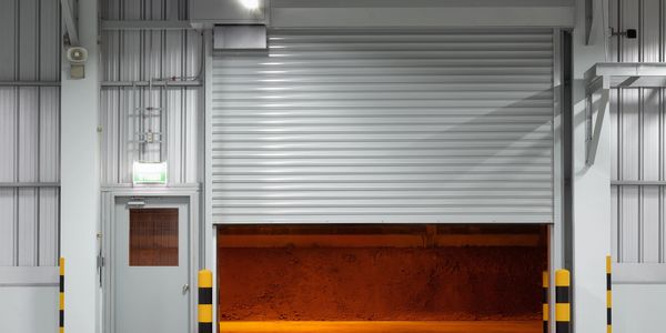 Partially opened industrial rolling door with orange light inside.