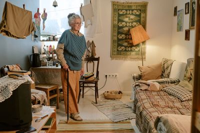 An elderly woman standing with a cane in a cozy living room.