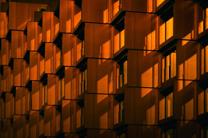 Modern residential facade with stacked orange balconies casting strong geometric shadows, modern residential complex