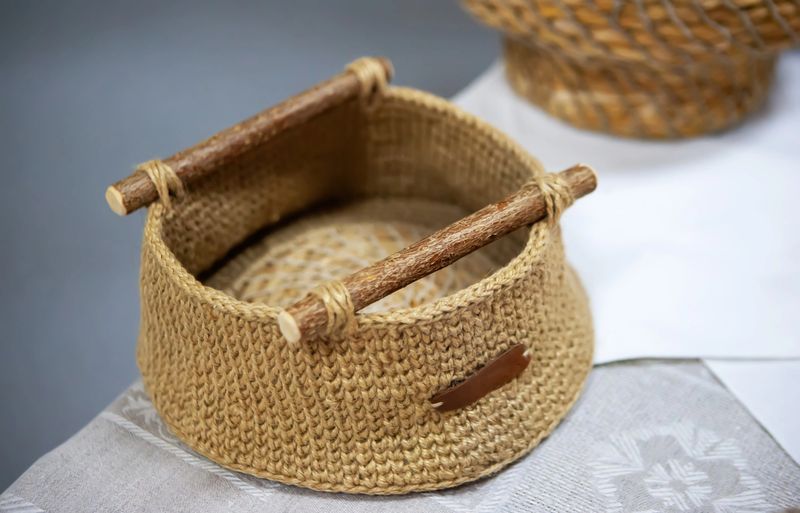 A beautiful wicker basket featuring sturdy wooden handles is elegantly presented on a textured textile surface, showcasing craftsmanship.