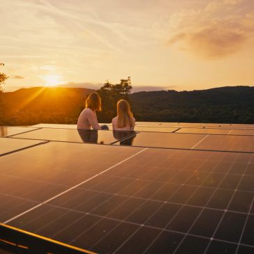 Two people sitting by solar panels during a golden sunset.