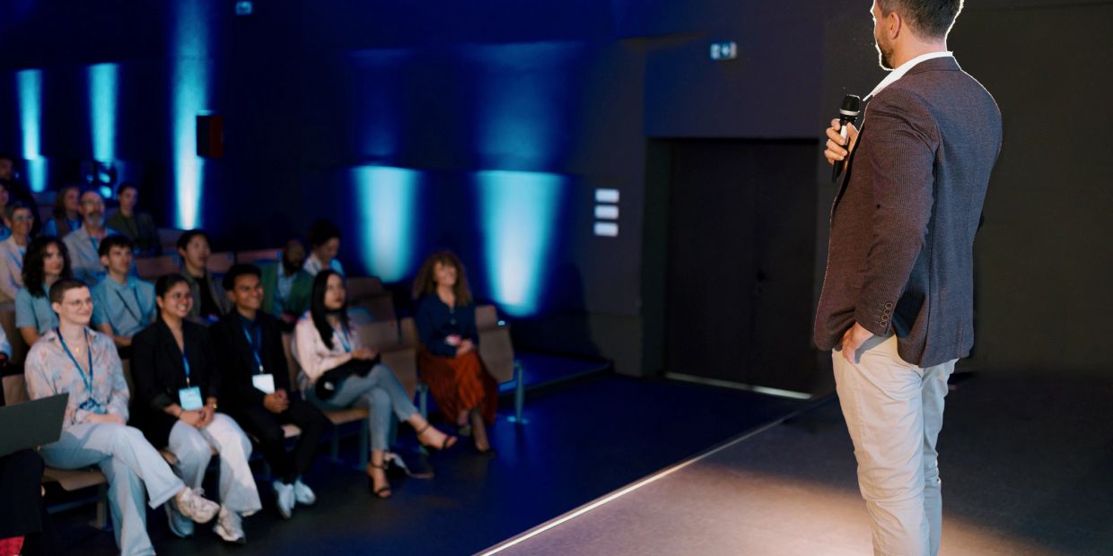 Man giving a presentation to an attentive audience in a dimly lit room.