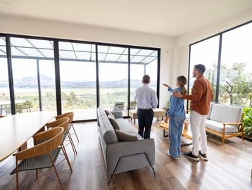 Couple and agent viewing a house with large windows.