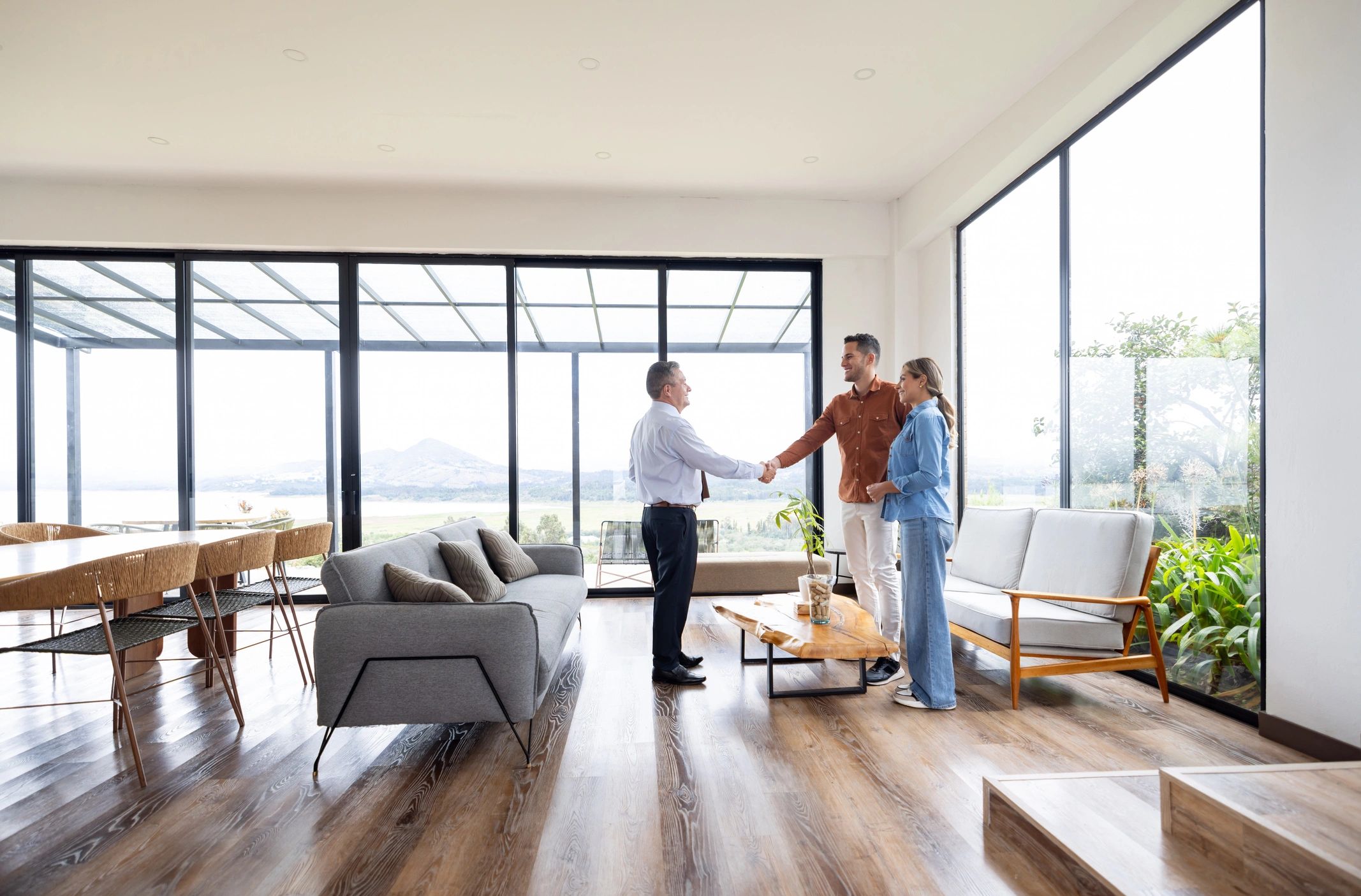 Couple shaking hands with a real estate agent in a bright living room.