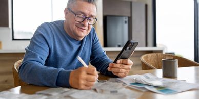Man multitasking with phone and paperwork at home.