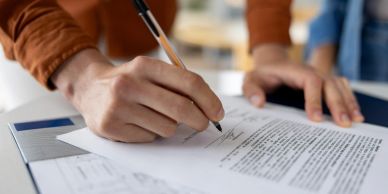 Person signing a document with a pen on a desk.