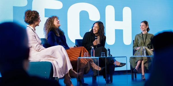 Four women discussing on stage at a tech event.