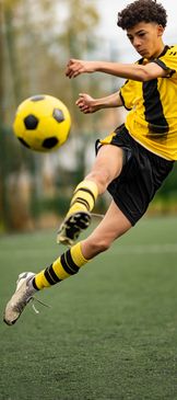 Young soccer player in yellow and black jersey kicking a ball mid-air.